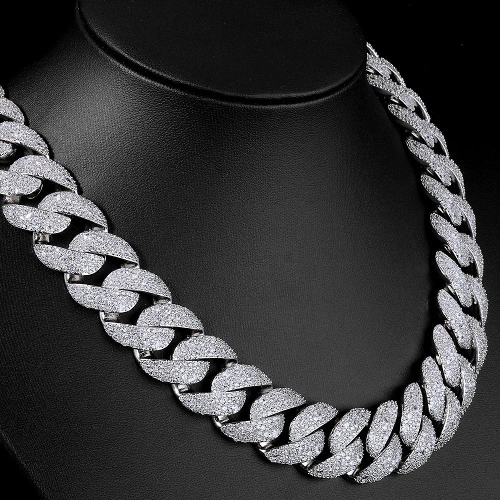 A close-up of a silver-toned Cuban link necklace with a curved flip buckle design displayed on a black display stand.