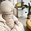 Beige Daunenjacke für Hund oder Katze liegt auf weißer Oberfläche.