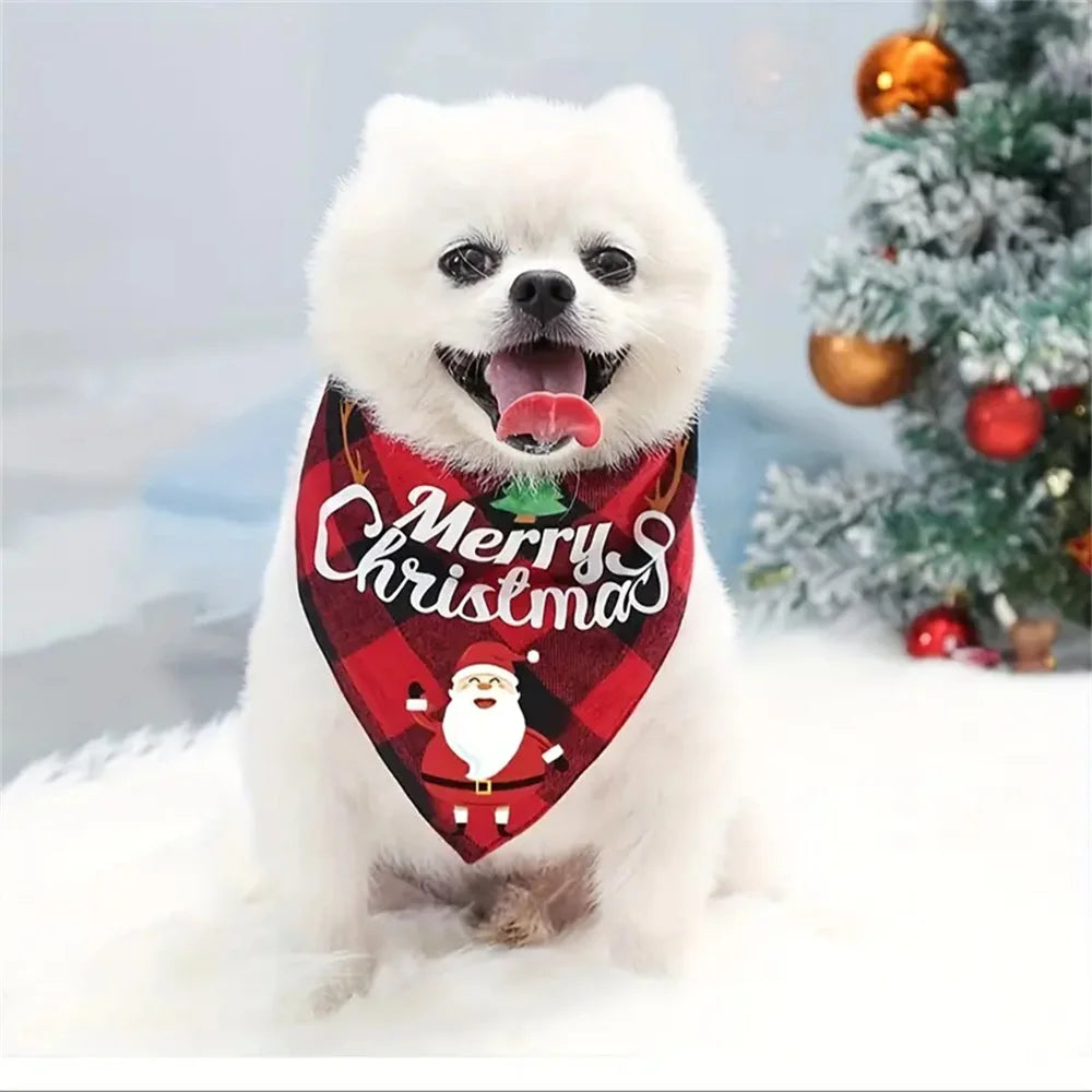A white dog wearing a red Christmas triangle scarf bandana with a Santa design in a snowy setting.