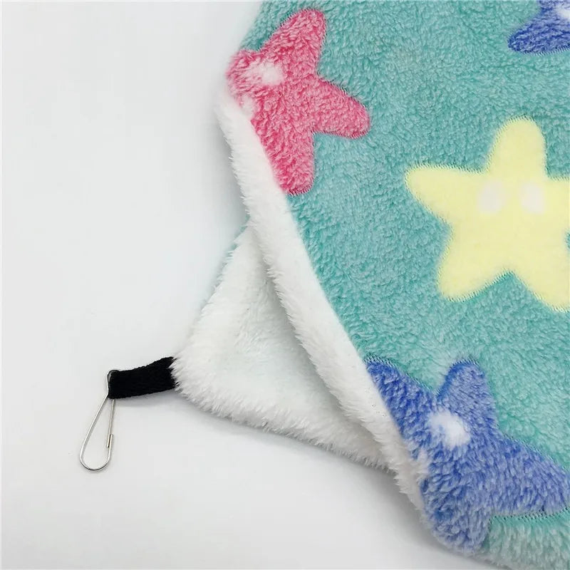 A soft, fuzzy green fleece hammock bed with pink and yellow star accents and a black strap.