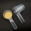 A transparent pet measuring spoon with a scale is shown next to a clear plastic container filled with yellow kibble.