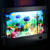 Aquarium en verre rempli de poissons et plantes tropicales colorés, illuminé par une veilleuse.