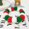 A circular pet collar made of red, white, and green fuzzy material with a bow tie visible in the background.