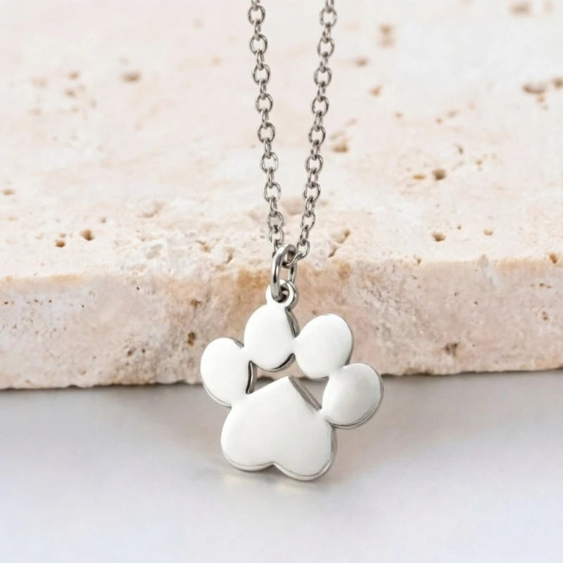 Silver stainless steel cat paw pendant necklace resting on a light stone surface