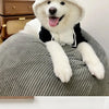A white dog wearing a black and white panda-themed fleece hooded coat is resting on a gray fabric surface.