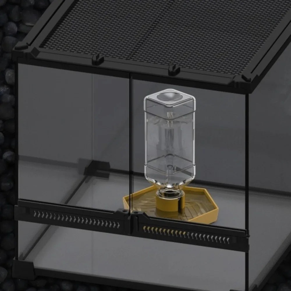 A clear glass water dispenser bowl sits on a yellow platform inside a black enclosure.