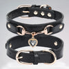 A black leather dog collar with a rose gold buckle and a clear rhinestone heart charm.