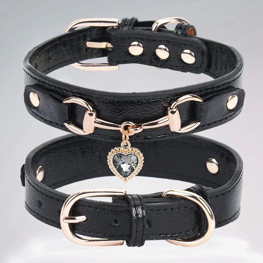 A black leather dog collar with a rose gold buckle and a clear rhinestone heart charm.