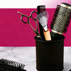 A black container holds various hair tools including scissors, a brush, and a round brush against a pink background.