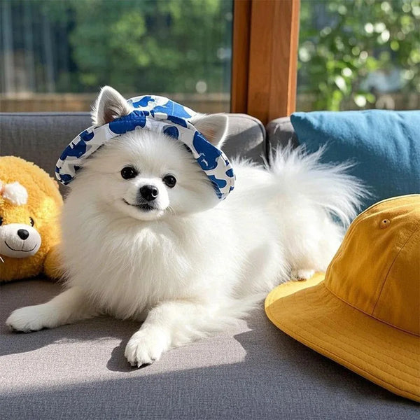 A fluffy white dog wearing a blue patterned bucket hat relaxing on a gray sofa.