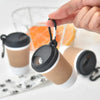 A hand is holding a portable pet poop trash can dispenser with a black and beige body and white lid.