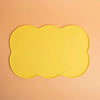 A bright yellow silicone pet feeding mat with a scalloped edge against a light peach background.