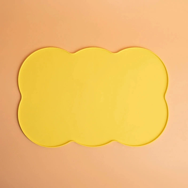 A bright yellow silicone pet feeding mat with a scalloped edge against a light peach background.