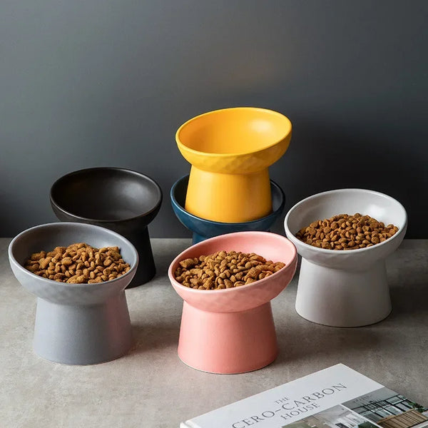 A collection of yellow, black, and pink ceramic bowls for pet food and water are displayed on a neutral surface.