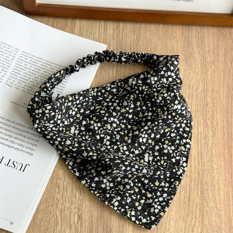 Diadema de tela negra con un pequeño estampado floral blanco y amarillo sobre una superficie de madera.