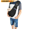 A person is wearing a black adjustable crossbody dog sling carrier with a small stuffed toy attached.