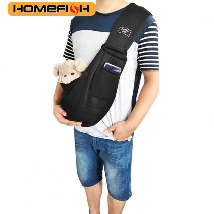 A person is wearing a black adjustable crossbody dog sling carrier with a small stuffed toy attached.