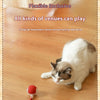 A white and gray cat is playing with a red string toy ball on a wooden floor.