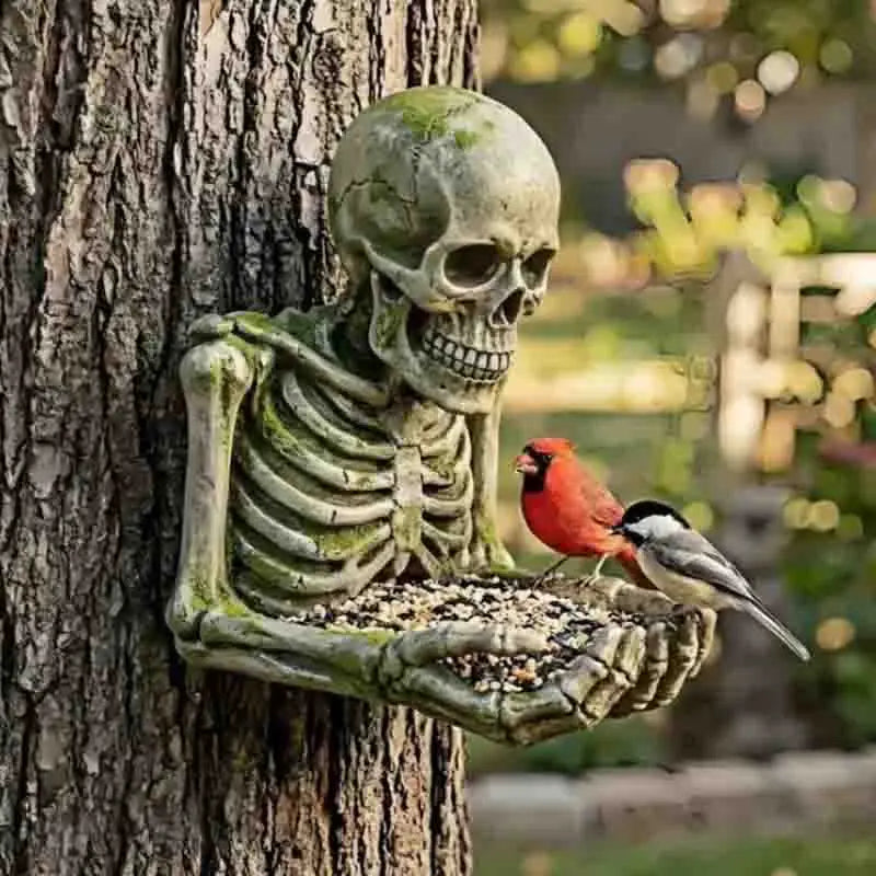 A sculpted skull and skeleton figure made of resin is attached to a tree trunk, serving as an outdoor garden decoration.