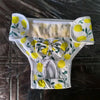 White dog diaper pants with yellow citrus print and a bow on a dark surface.