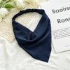 A navy blue fabric scarf tied in a knot, displayed on a light background next to a piece of paper.