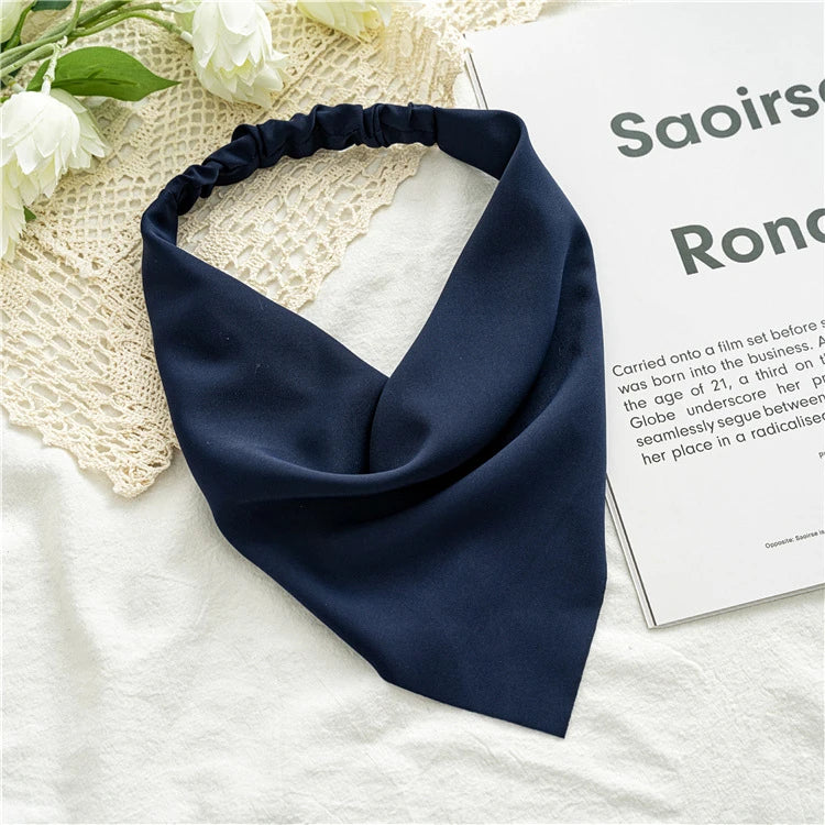 A navy blue fabric scarf tied in a knot, displayed on a light background next to a piece of paper.