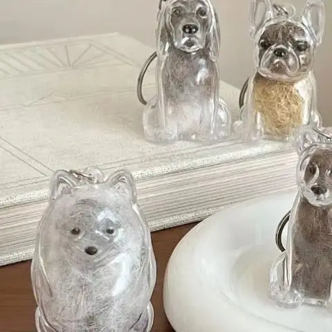 Clear glass dog hair storage keychain pendants displayed on a white surface.