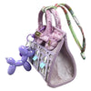 A handcrafted mini house-shaped bag in lavender with a puppy keychain charm and green patterned strap.