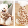 A fluffy white dog wearing a leopard print dress with a white fluffy collar.