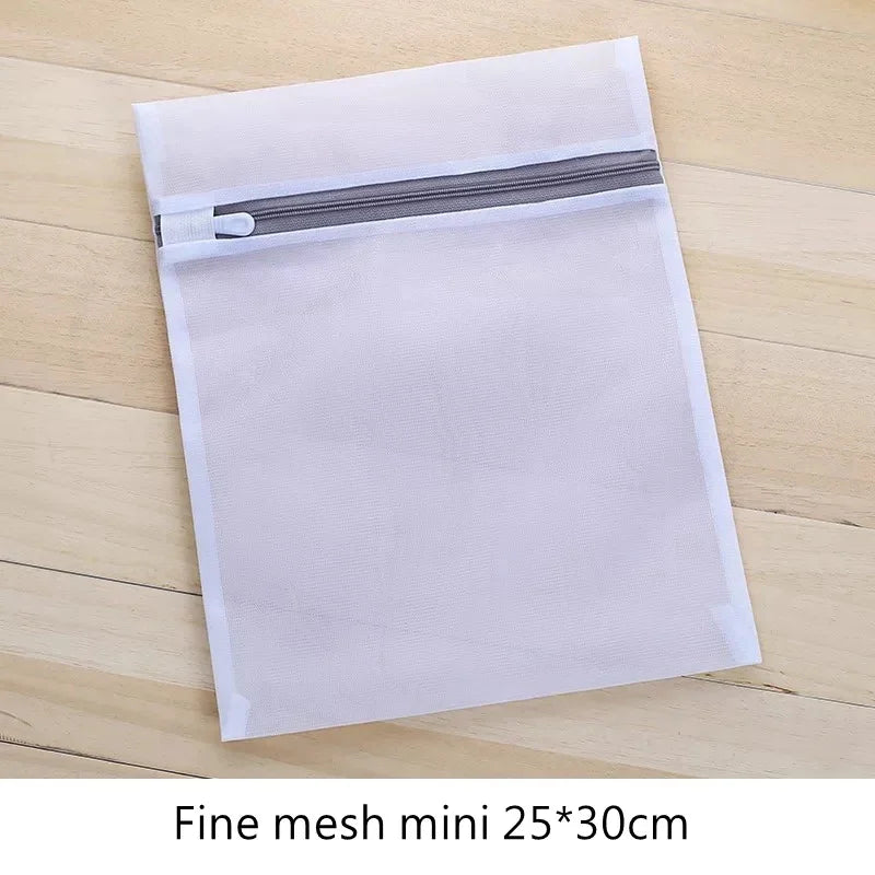 Una bolsa de ropa de malla transparente con cremallera gris mostrada sobre una superficie de madera.