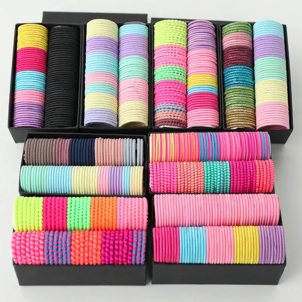 A collection of colorful elastic hair bands in various shades of pink, purple, green, and yellow are displayed in black packa