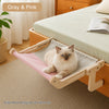 A solid wood hanging cat hammock in pink and gray fabric resting on a wooden bed frame.