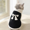 A gray cat wearing a black ribbed pet vest with a white bow knot.
