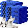 Eine Stapel blaue Mikrofaser-Tierbadtücher mit schwarzen Pfotenabdruck-Designs neben einem weißen Hund.