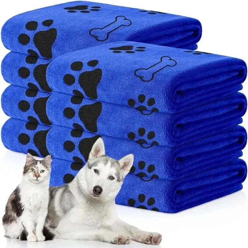 Eine Stapel blaue Mikrofaser-Tierbadtücher mit schwarzen Pfotenabdruck-Designs neben einem weißen Hund.