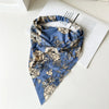 Diadema o pañuelo para el cabello de elástico con estampado floral azul y beige, sobre una superficie blanca junto a un libro