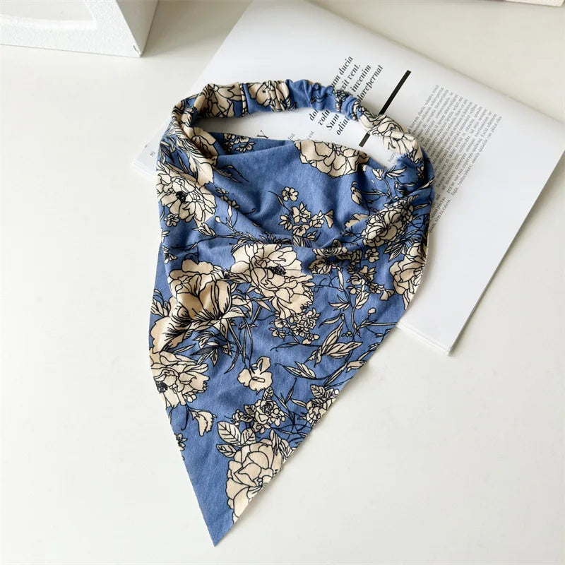 Diadema o pañuelo para el cabello de elástico con estampado floral azul y beige, sobre una superficie blanca junto a un libro