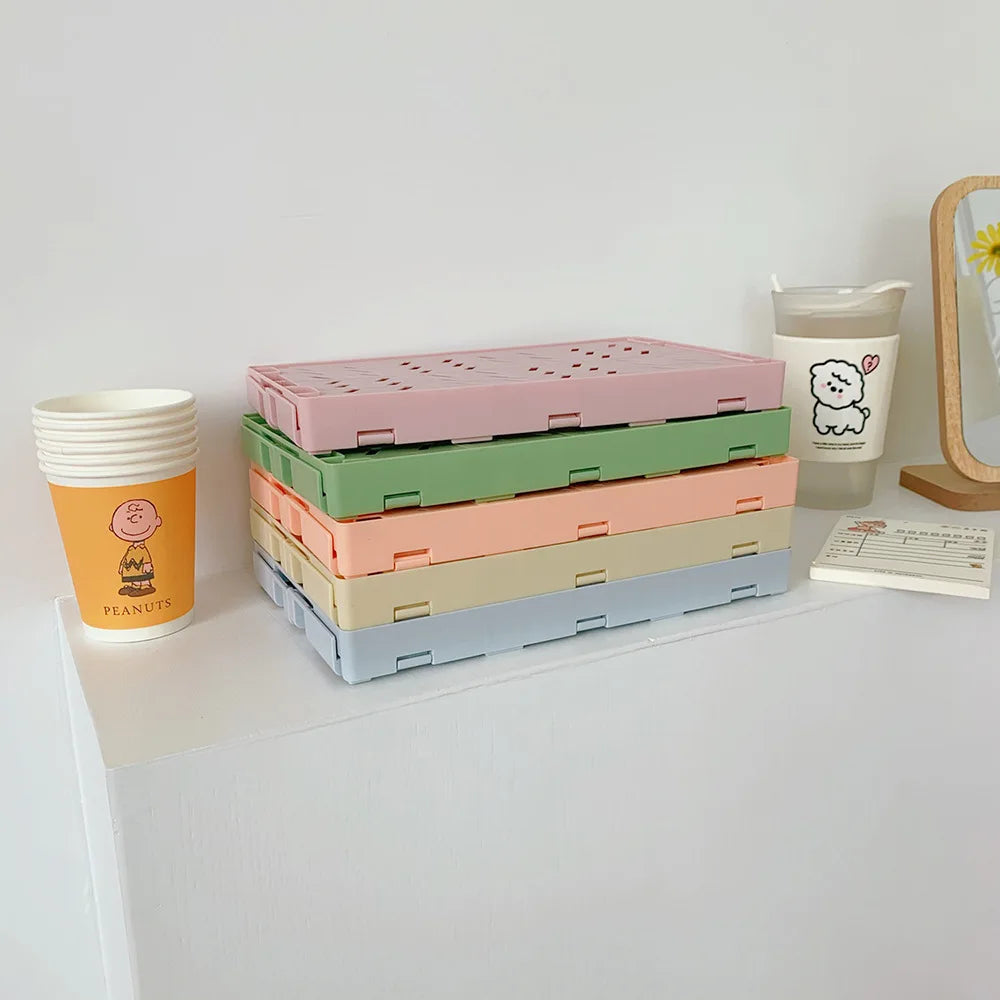 Gestapelte, farbenfrohe, faltbare Plastik-Aufbewahrungskörbe in rosa, grün und beige auf einem weißen Regal.