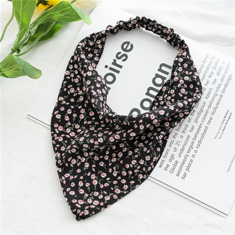 Diadema elástica o pañuelo para el pelo con estampado floral negro, mostrada sobre un fondo blanco junto a una revista.