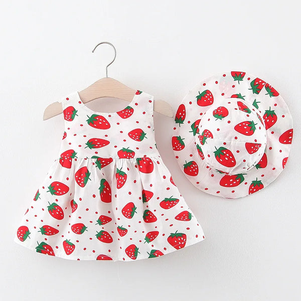 Weißes Sommerkleid und passende Mütze mit roter Erdbeere-Muster, auf einem Holzbügel