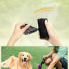 Manos sosteniendo una bolsa de basura portátil negra para mascotas y un golden retriever tumbado en césped verde.