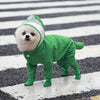 Un chien blanc et duveteux portant un imperméable vert marchant sur un trottoir mouillé.