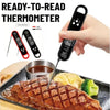 A hand holds a digital meat thermometer measuring a steak on a grill plate.