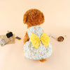 A fluffy brown dog wearing a light blue and white floral summer bow dress with a yellow bow.