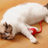 A white and gray cat is lying on a wooden floor next to a red interactive cat toy ball.