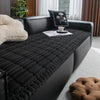 A black plaid flannel pet seat protector and car mat placed on a dark leather sofa.