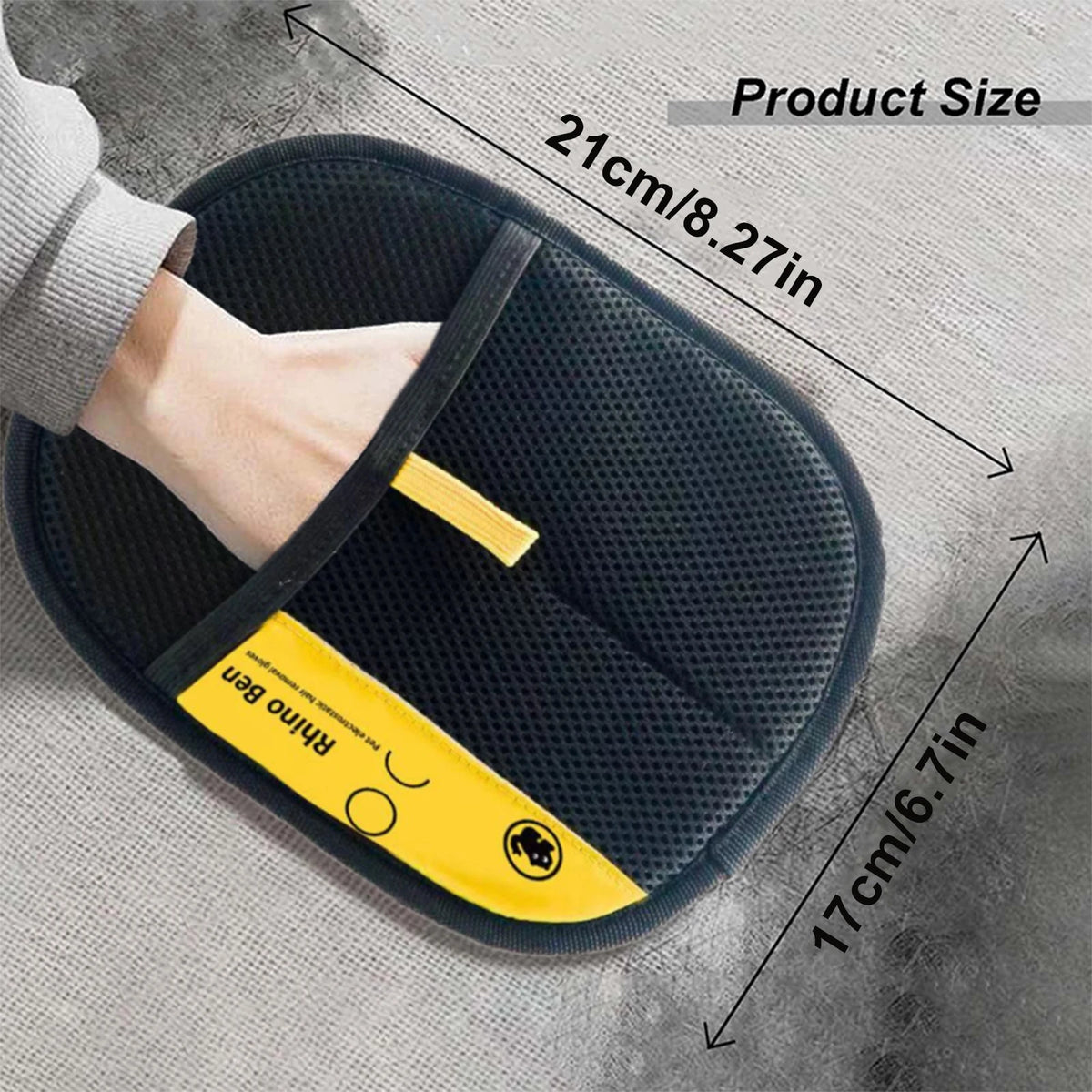 A hand is holding a black silicone pet hair removal glove with yellow accents on a gray fabric background.