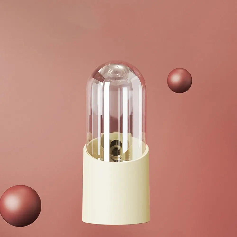 Klares Glasvogelfutter mit weißer Basis und pinker Kugel, vor rosigem Hintergrund.
