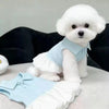 A fluffy white puppy wearing a light blue polo dress and matching bottoms.