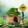 A resin aquarium house decor with a green roof and wooden entrance, featuring a small orange squirrel nearby.